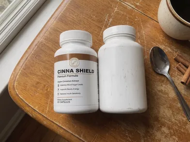 CinnaShield bottle next to a plain unlabeled white supplement bottle on a wooden table